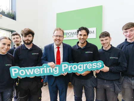 A group of Powercomm Apprentices at Grand Opening with Minister James Lawless holding up a sign saying Powering Progress