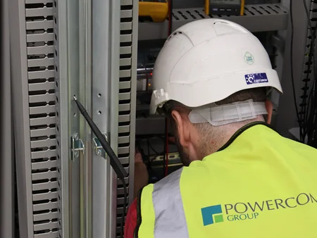 Engineer with high viz and helmet working on an electrical board