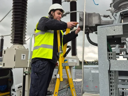 Young man standing on a ladder with his PPE gear on, using equipment