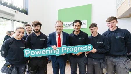 A group of Powercomm Apprentices at Grand Opening with Minister James Lawless holding up a sign saying Powering Progress