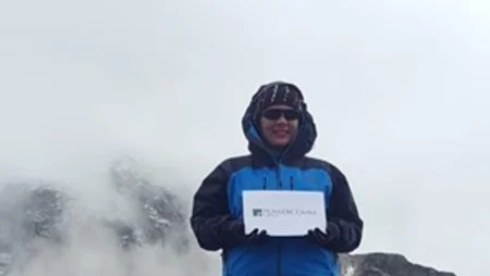 Grainne Rouleau standing and holding white paper with Powercomm logo on top of Mount Everest.