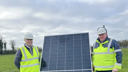 Martin Eager (left) and James Cafferty (right) stand on a green field at Solar Farm Ballycore . A solar panel is positioned between them.