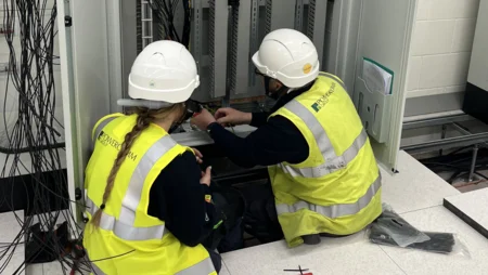 A person in charge of works mentoring an apprentice electrician on how to terminate a panel