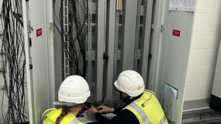 A person in charge of works mentoring an apprentice electrician on how to terminate a panel