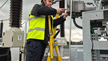 Young man standing on a ladder with his PPE gear on, using equipment